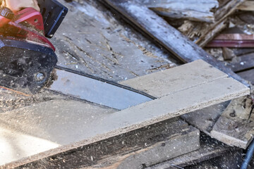 Cutting old wooden chipboards with electric chainsaw, splinters flying in air, closeup detail