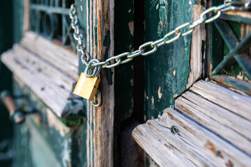 Wooden shabby green door locked with golden padlock. The doors of the old house are locked. Property locked with chain.