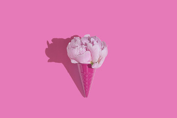 Creative pink toy ice cream cone with pink peony fluffy flower on pink minimal background with copy space flat lay. Botany idea for summer or spring wallpaper or greeting card.