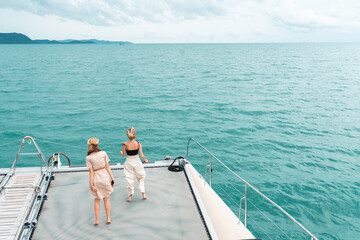 In the back two Caucasian women tourists standing and jumping in front of the catamaran yacht with...