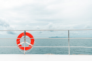 Orange color life buoy hanging on the rail of the luxury catamaran yacht with sea and sky in the background. Safety equipment for tourists and drivers.