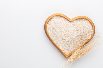 Wheat flour in a wooden heart shape bowl on a pastel background.