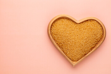Brown sugar in heart wooden bowl shape on pasttel background.