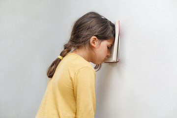 Sad and tired caucasian girl with dyslexia holds a wall. The child learns to speak and read...