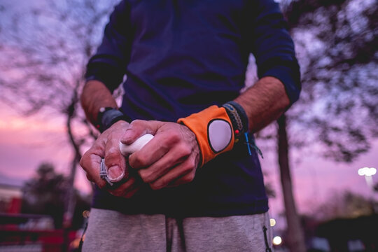 Close up of hands of a healthy and fit young latin man with wristbands holding a bag of magnesium on a street workout park with beautiful and colorful sunset sky