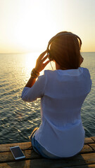 Young beautiful girl listening to music(radio) on headphones on the beach near the sea - 514250094