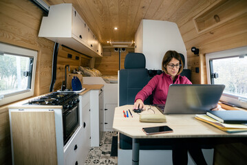 Vanlife. Woman doing remote work with the computer in the motorhome.