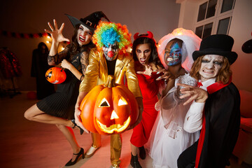 Group of young happy friends in costumes on Halloween having fun at party making scary faces....