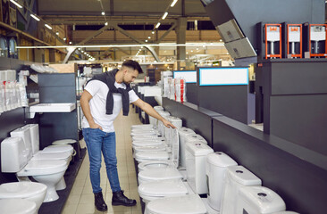 Male customer looking at white flush toilets on sale at a modern store or shopping centre. Young...