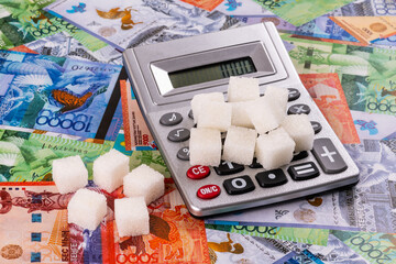 Pieces of refined sugar and a calculator on the background of Kazakh banknotes - tenge