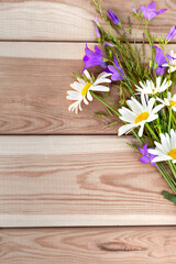 Flowers of bluebells and daisies on a light wooden background in the form of a bouquet. Congratulations. Holiday. Birthday. A flat copy space with a top view.