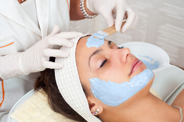 Woman lying on massage table in health spa while facial mask is applied on her face