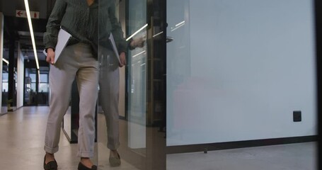 Biracial businesswoman walking with laptop and opening door at office