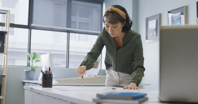Biracial businesswoman working with schema and compass alone at office