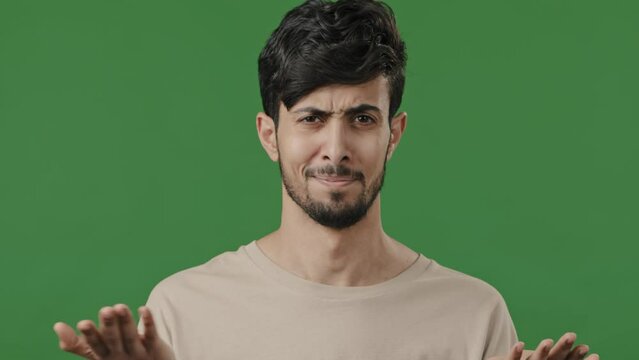 Dissatisfied shocked young man 20s guy wears casual shirt bemused asks what show displeased emotion swing hands feels aversion make frowning face grimacing isolated on green background studio portrait
