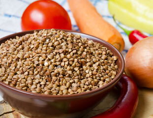 Buckwheat in a bowl, red peppers, carrots and onions on a board.