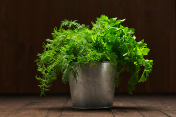a bunch of green dill and parsley in an iron bucket, dark wooden background, concept of fresh vegetables and healthy food