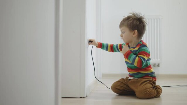 Small boy playing with electrical plug into the wall socket, unsafe activity