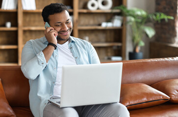 Indian freelancer guy in casual wear using laptop computer for remote work and talking on the...