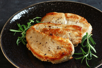 Fried pork steaks on a black plate on a dark background with rosemary close up