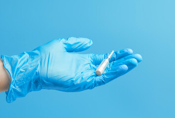 Medical glove. An ampoule with a white liquid in his hand in a blue medical glove. Isolated on a blue background.