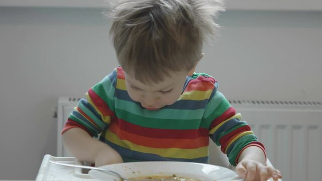 Hungry little kid eating soup with noodles with big spoon