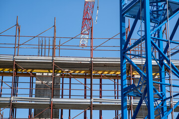 construction site of a building: a hoist with the scaffolding and part of a crane with its hook that lifts tons of material from one floor to another on the construction site.