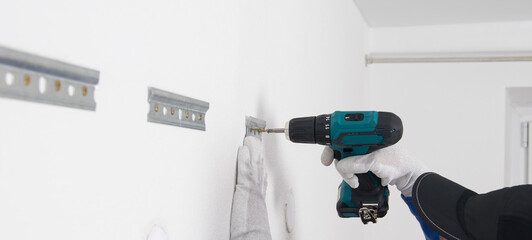 the hands of the worker, against the background of a white wall, fasten the bracket for hanging furniture