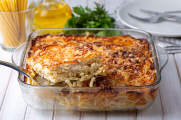 Pasta casserole bechamel sauce topped with melted mozzarella cheese and served in a white baking dish on a table (Turkish name; firinda makarna or firin makarna)