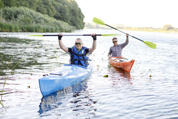 Two adult men is sitting in a kayak and greetings. The concept of the water activities.