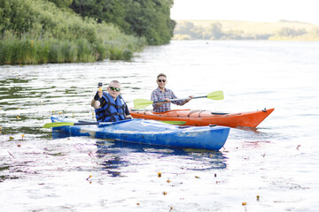 Two young men sit in kayaks and take a selfie with a portable camera. The concept of water entertainment.
