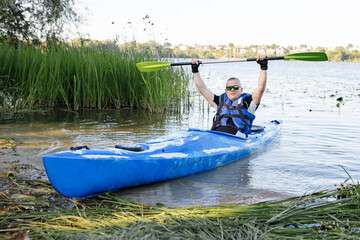 Adult caucasian man is sitting in a kayak and greetings. The concept of the water activities.