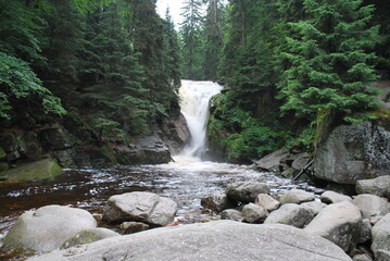 Szklarki waterfall in the Karkonosze Mountains, Poland. A view of a waterfall surrounded by a forest on a cloudy day. © TK_Office