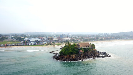 Small island off the coast of Sri Lanka seen from above. Located in the souther part of Sri Lanka, with a temple on the island, connected by a suspended bridge from the mainland