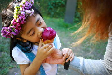 The little girl is cute and enjoying eating ice cream. Asian kid in beautiful garden.