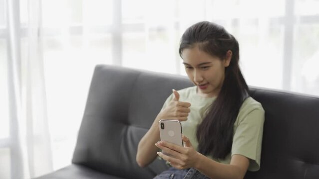 View of Asian woman using smartphone to chat with friends online on Sopa at home, 4k video.