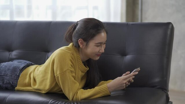 View of Asian woman using smartphone to chat with friends online on Sopa at home, 4k video.