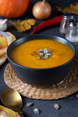 Thick pumpkin cream soup with pumpkin seeds in dark bowl on gray background