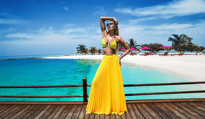 Elegant tanned woman in yellow bikini and long skirt on tropical beach on Maldives island. Summer...