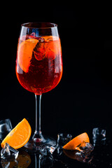Shining cocktail Aperol syringe in a wine glass with ice and a slice of orange on a dark background