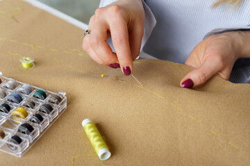 Tailor with needle in hands sews clothing. Woman seamstress at workplace. Closeup needlework