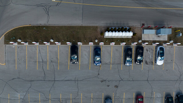 A direct overhead aerial view above a Tesla Supercharger station, cars are seen parked, charging during the day.