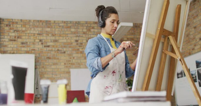 Video of biracial female artist in headphones painting in studio