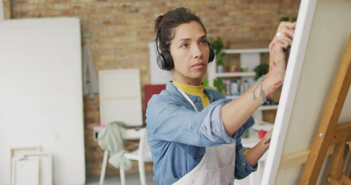 Video of biracial female artist in headphones painting in studio