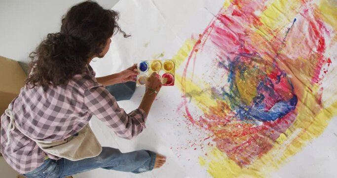 Video of biracial female artist painting on floor in studio