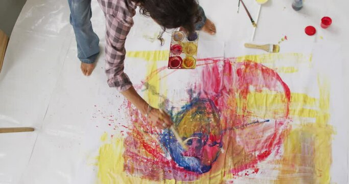Video of biracial female artist painting on floor in studio