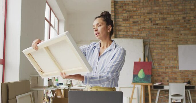 Video of happy biracial female artist looking at painting in studio