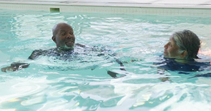 Video of happy senior african american couple swimming in pool