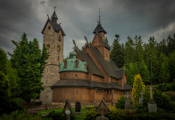 Fototapeta na wymiar Wooden church with stone tower in cloudy spring day in Karpacz town