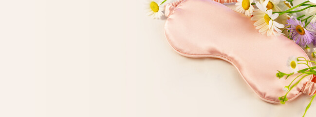 Concept of Good morning, no depression, good sleep and self-care. Banner with pink sleeping mask with wild flowers on a white bed linen with copy space. Soft focus style, banner size